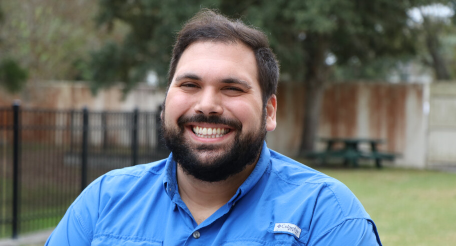 A man with a beard smiling in a blue shirt.