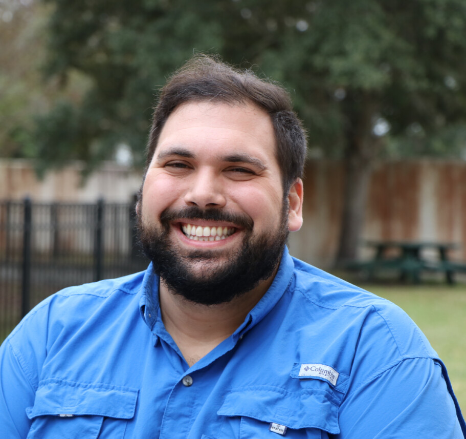 A man with a beard smiling in a blue shirt.