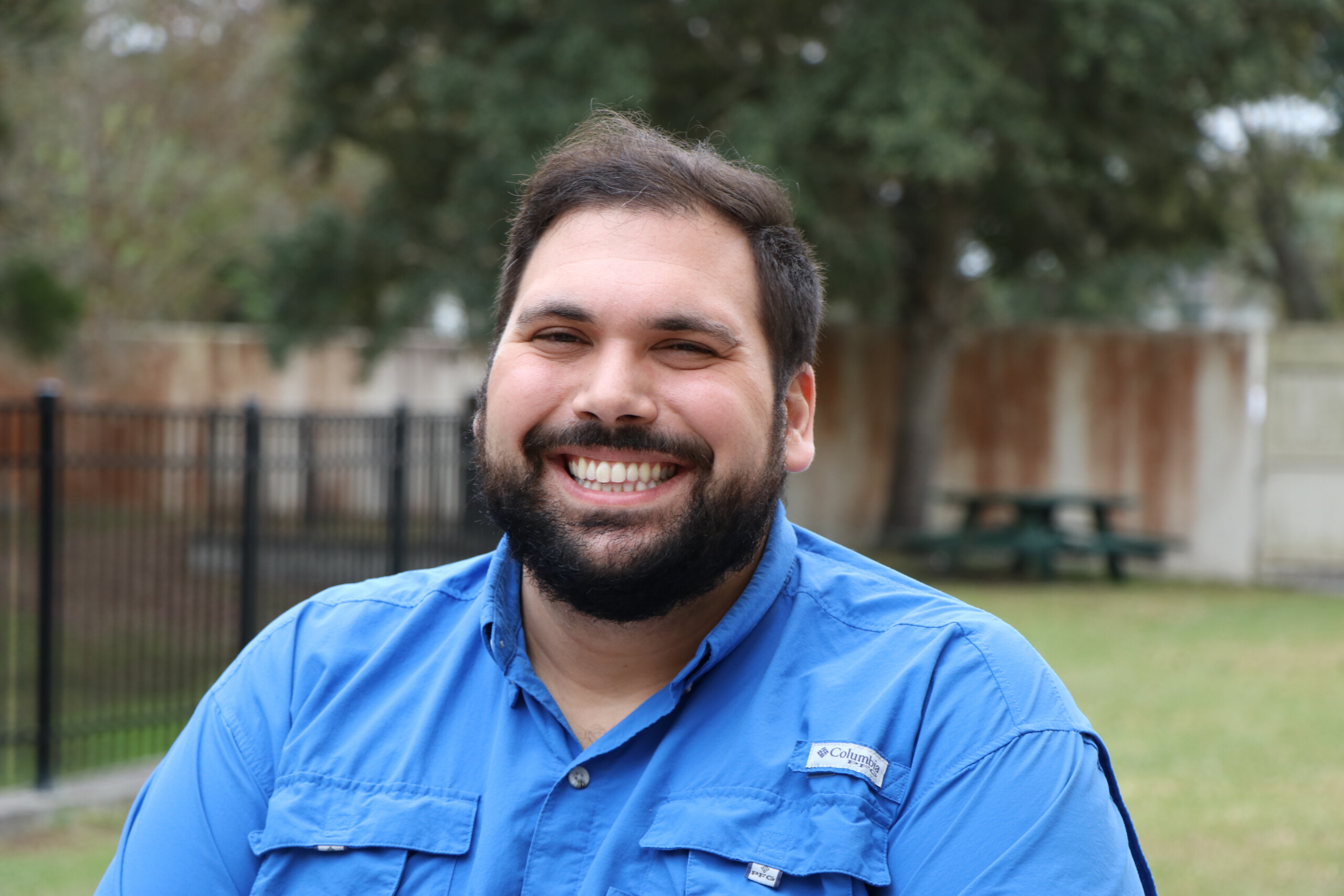 A man with a beard smiling in a blue shirt.