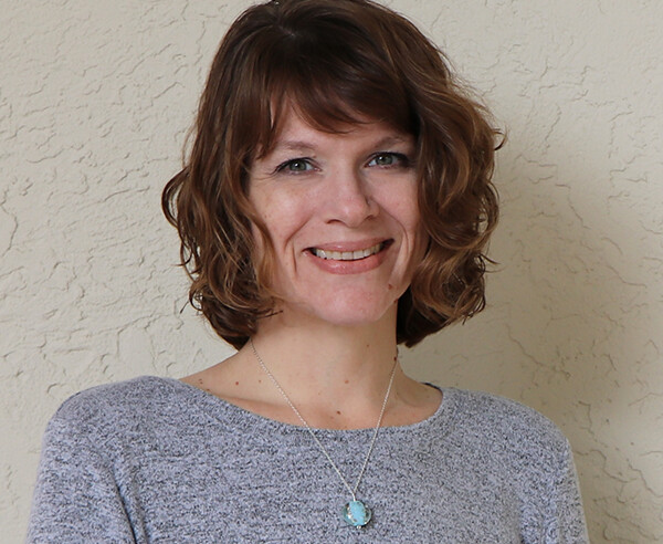 A woman wearing a gray sweater and a necklace.