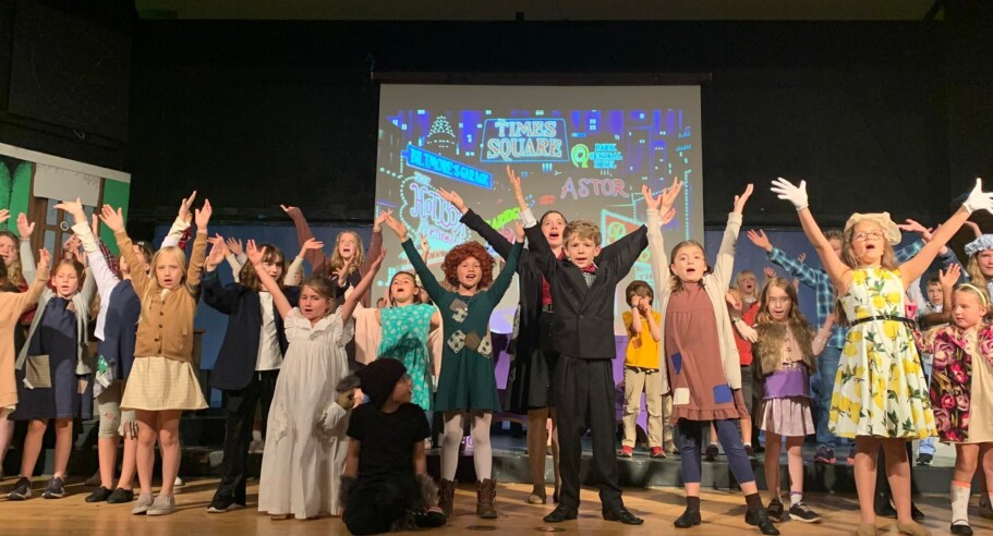 A group of children on stage with their hands up.