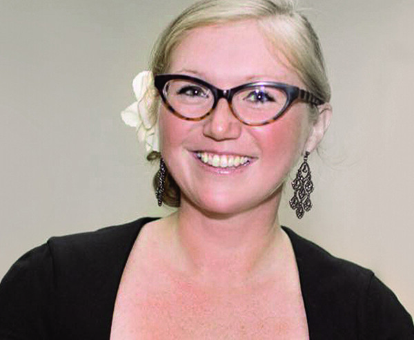 A smiling woman in glasses wearing a black top.