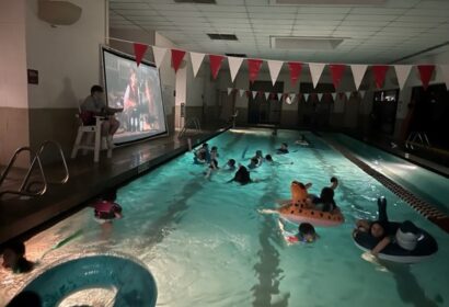 A group of youth floating in an indoor pool watching a movie.