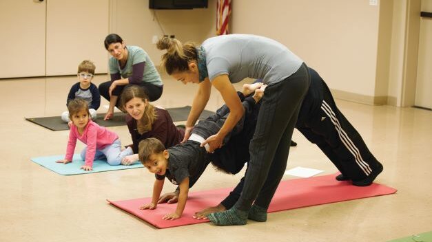 A group of people doing yoga in a room with children.