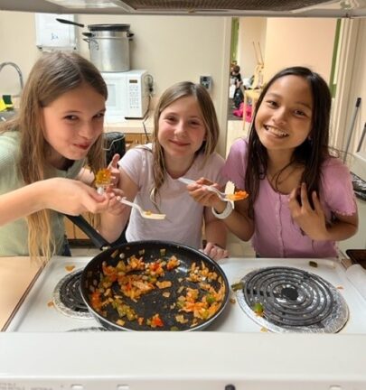 Three girls are preparing food in a kitchen.