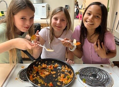 Three girls are preparing food in a kitchen.