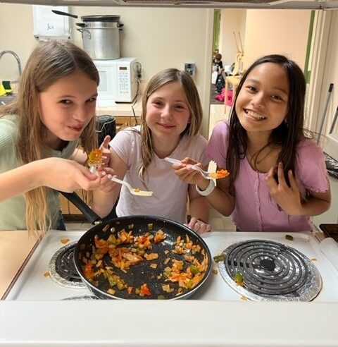 Three girls are preparing food in a kitchen.