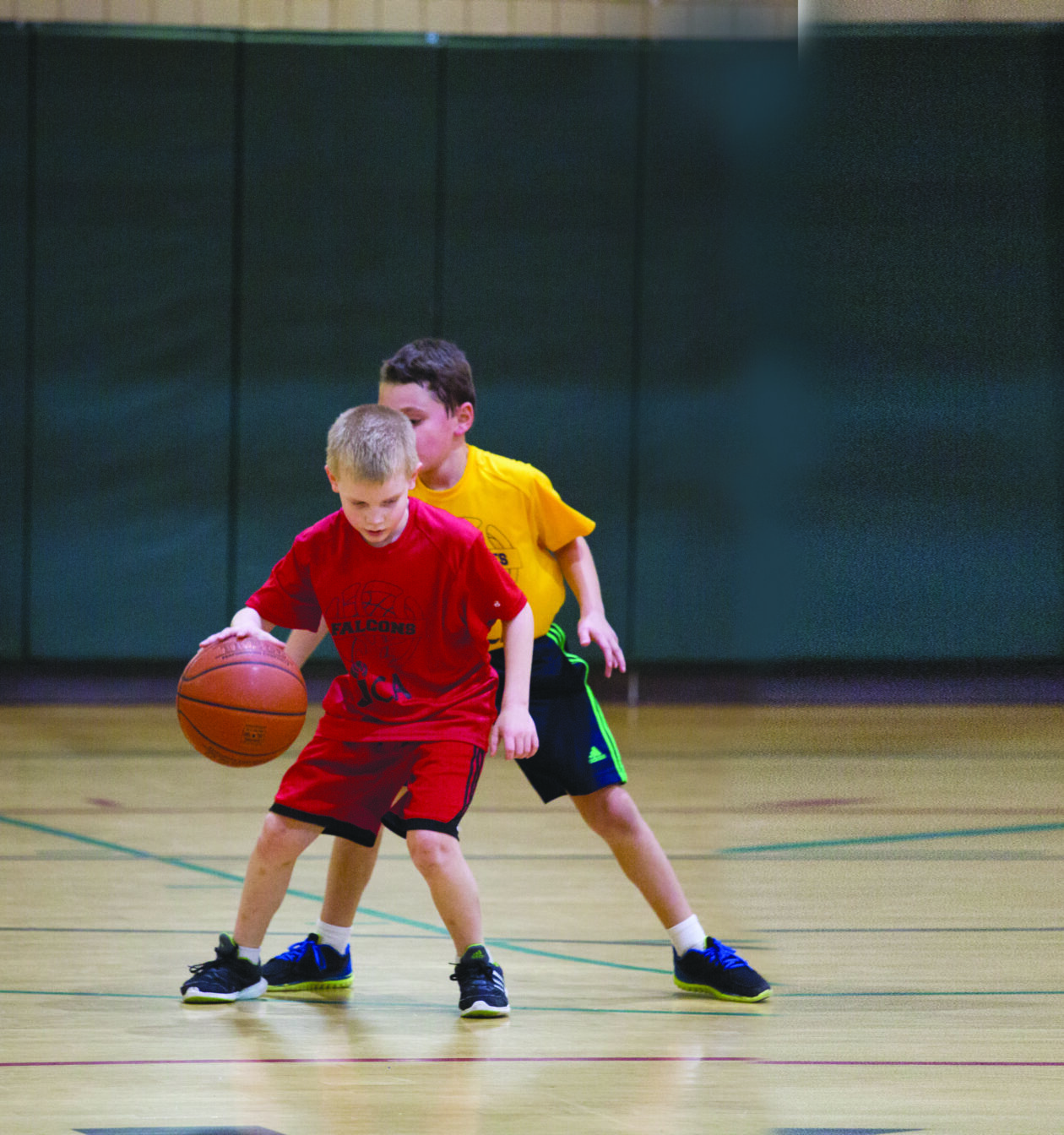 Two boys playing basketball in a gym.