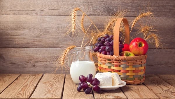 A basket with apples, grapes and milk on a wooden table.