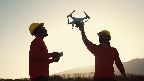 Two men in hard hats are holding up a drone.
