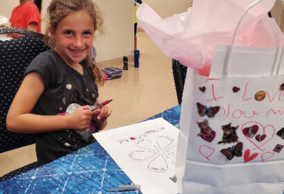 A young girl sitting at a table with a gift bag.