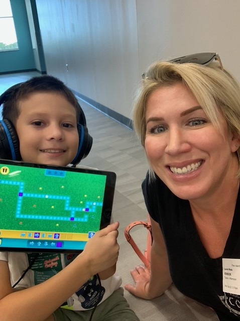A woman with headphones and a boy holding an ipad.