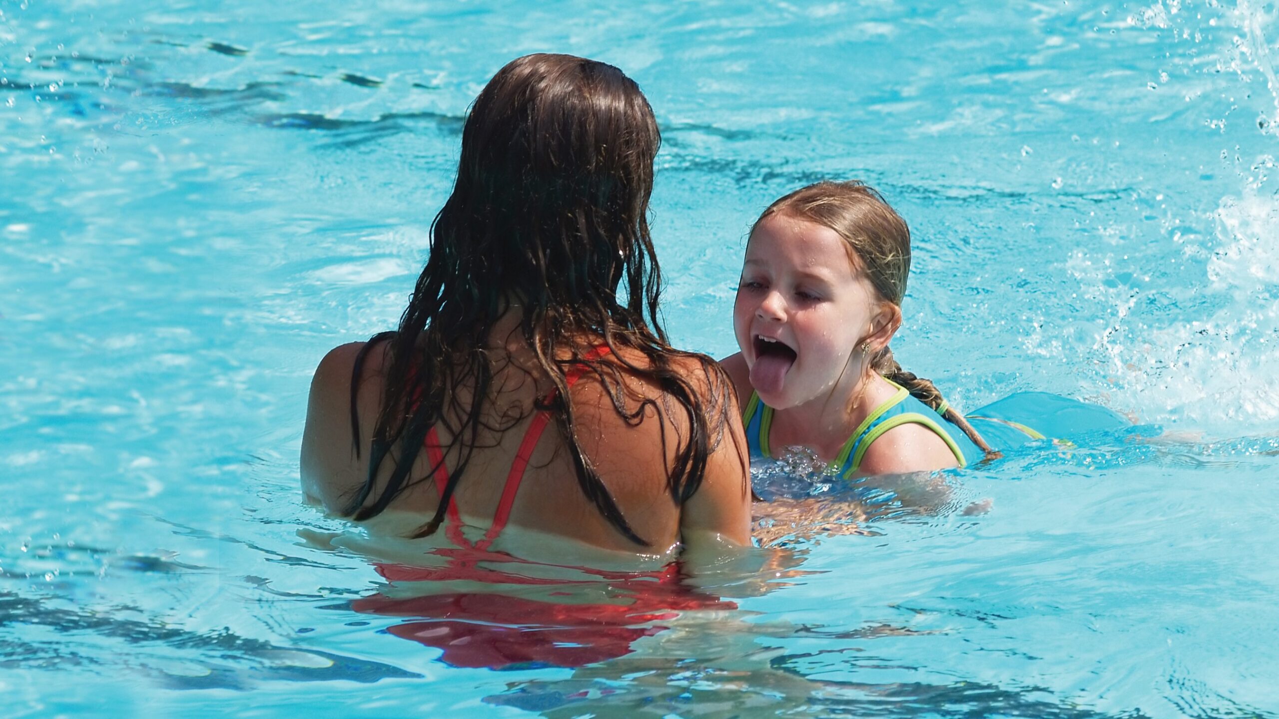 A young girl is swimming with her mother in a swimming pool.