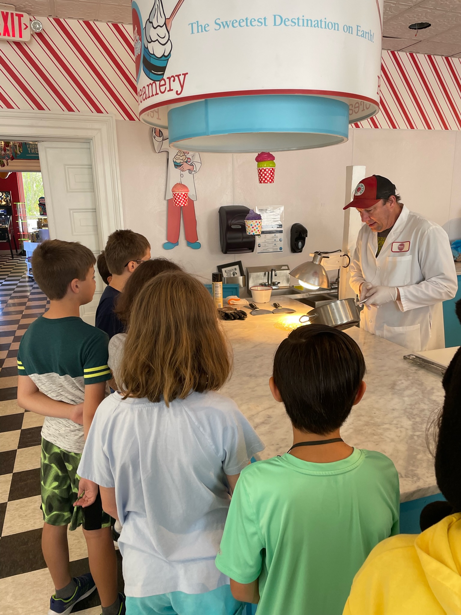 A group of children standing around a counter in a ice cream shop.
