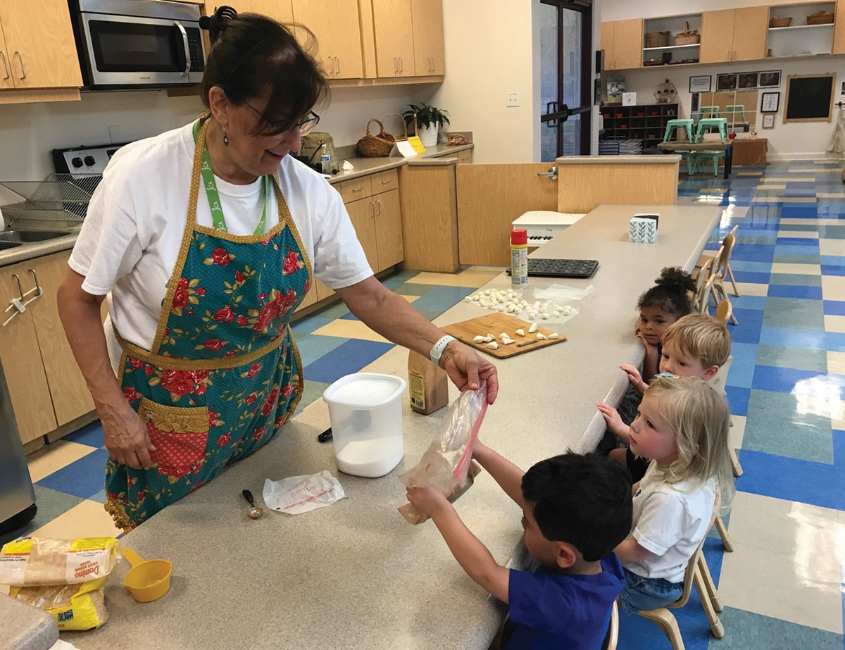 A woman in an apron is helping a group of children.