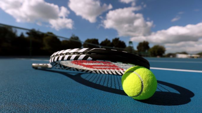 A tennis racket and ball on a blue tennis court.