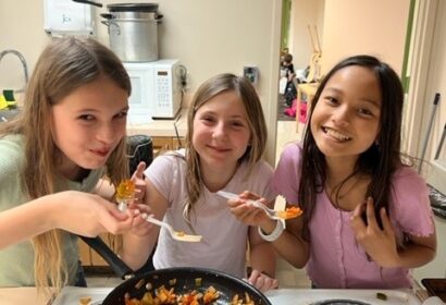 Three girls preparing food in a kitchen.