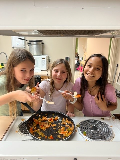 Three girls preparing food in a kitchen.