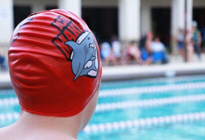 A boy wearing a red swim cap in front of a swimming pool.