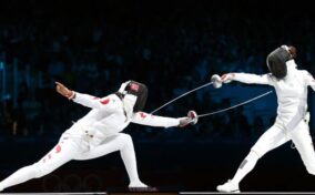 Two fencers in a fencing match at night.