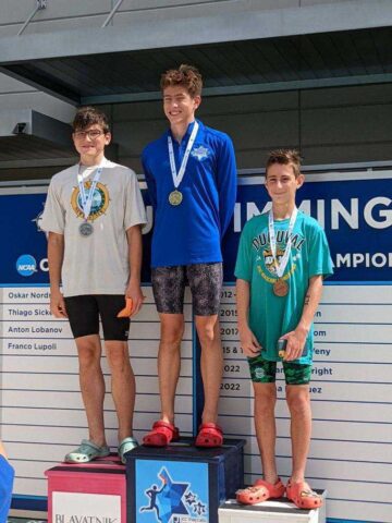 Three boys standing on a podium with medals.