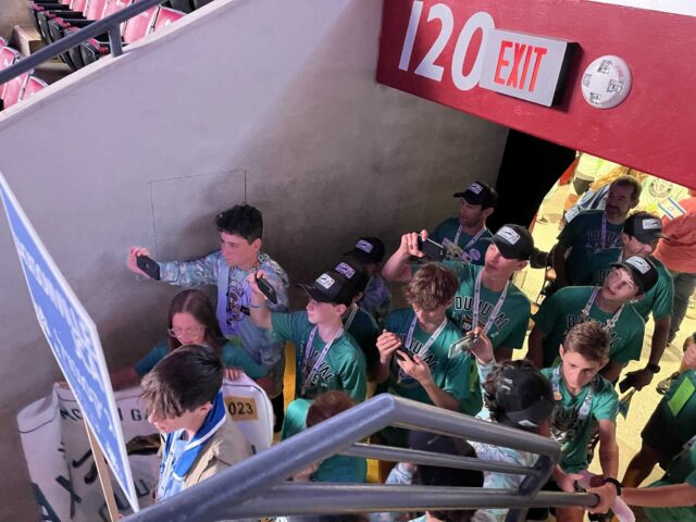 A group of people in green scout uniforms standing in an elevator.