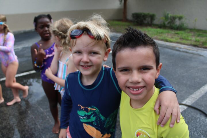 A group of kids in swimwear standing outdoors, with two boys in the foreground smiling at the camera.