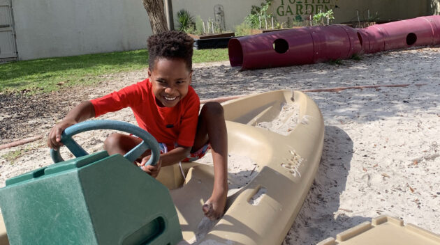 Boy smiling as he plays on the boat outside on the beach playground
