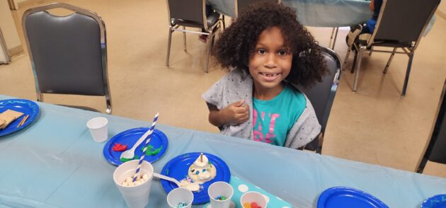 A young girl sitting at a table with plates and utensils.