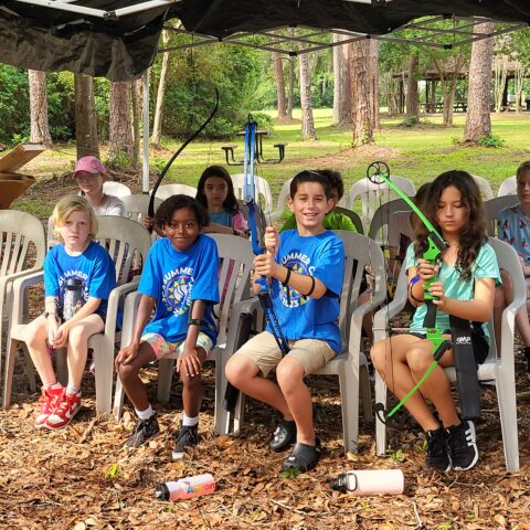 A group of kids sitting in chairs under a tent.