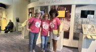 Three women in pink t - shirts standing in front of an exhibit.