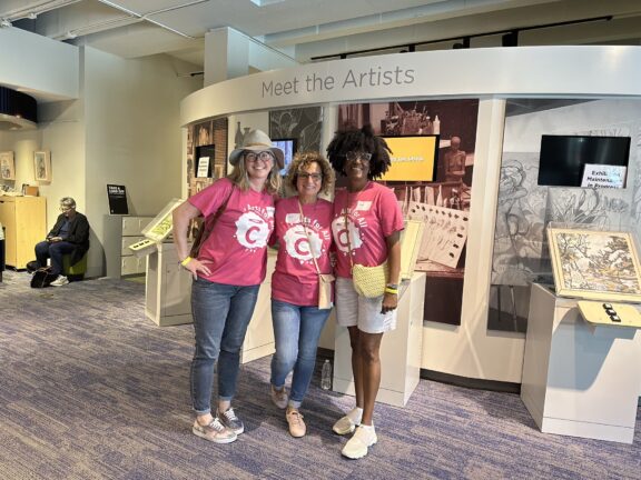 Three women in pink t - shirts standing in front of an exhibit.