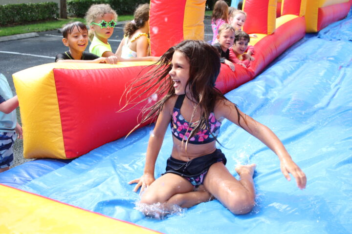 A girl is playing on a water slide at a party.