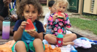 A group of children sitting on a blanket eating watermelon.