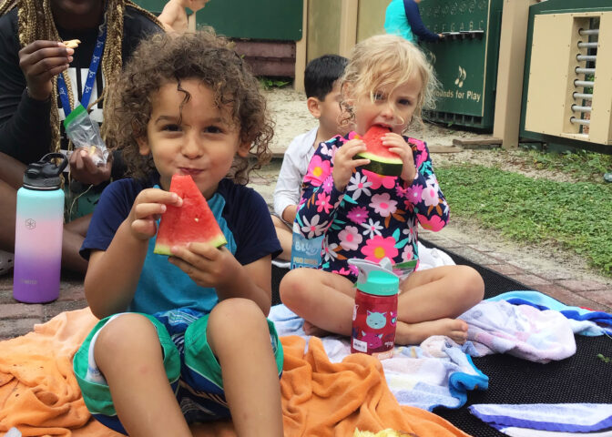 A group of children sitting on a blanket eating watermelon.