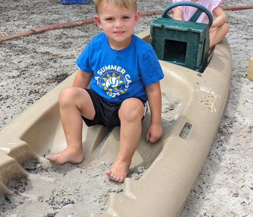 A boy and a girl sitting on a boat in a sand pit.