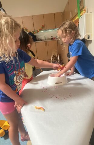 Two children play with plastic insects on a white table in a classroom.