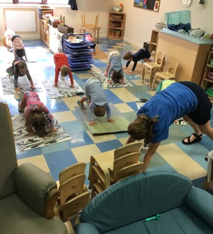 Children and an adult practicing yoga poses on mats in a classroom.