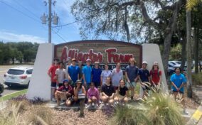 A group of people posing in front of the "St. Augustine Alligator Farm Zoological Park" sign on a sunny day.