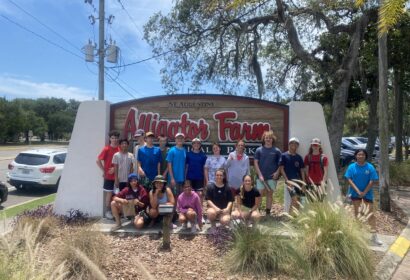 A group of people posing in front of the "St. Augustine Alligator Farm Zoological Park" sign on a sunny day.