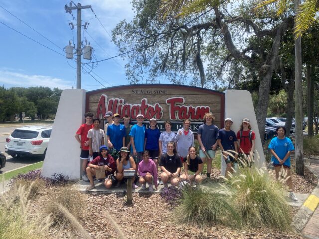 A group of people posing in front of the "St. Augustine Alligator Farm Zoological Park" sign on a sunny day.