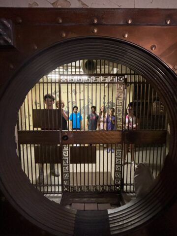 Group of people standing inside a room, seen through the large round door of a vault.