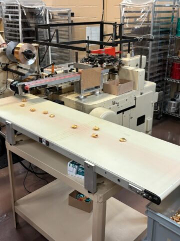 A packaging machine processes small wrapped candies on a conveyor belt in a factory setting.