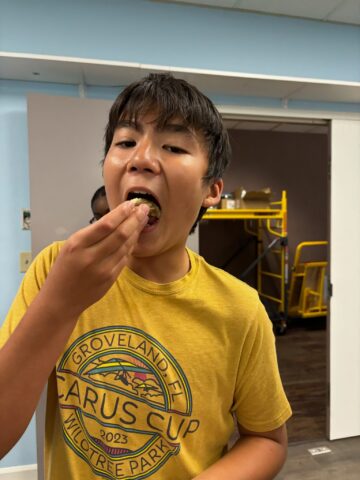 A boy in a yellow shirt is eating a donut in a room with a yellow cart in the background.