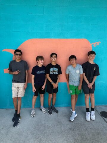 Five boys standing in front of a blue wall with a pink pig mural.