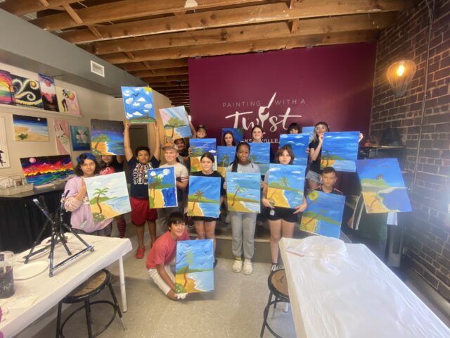 A group of people in a studio holding up paintings of tropical islands.