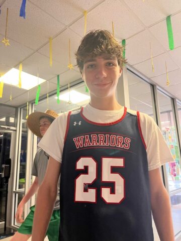 A young man in a basketball uniform standing in a hallway.