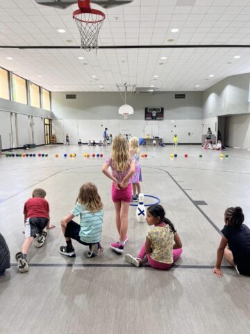 A group of children sitting on the floor in a gym.