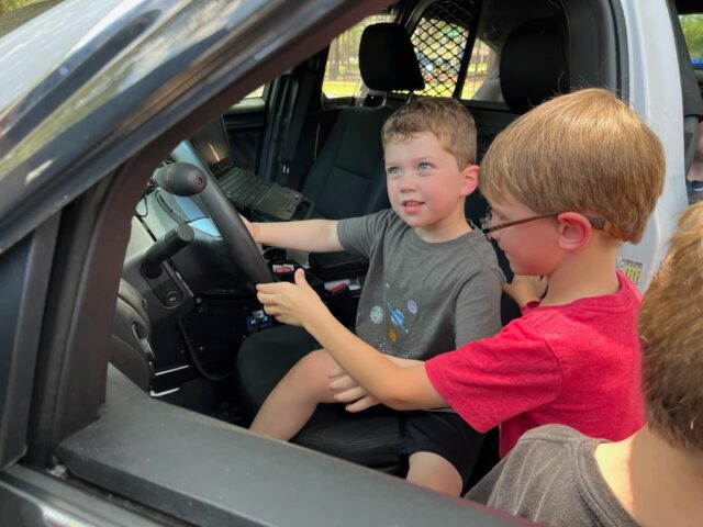 Two boys sitting in the driver's seat of a car.