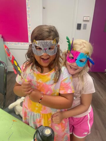 Two little girls wearing masks in a classroom.